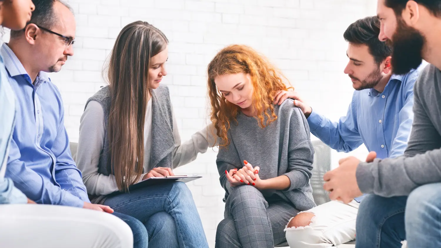 Mitglieder einer Selbsthilfegruppe trösten eine depressive Frau in einer Psychotherapiesitzung